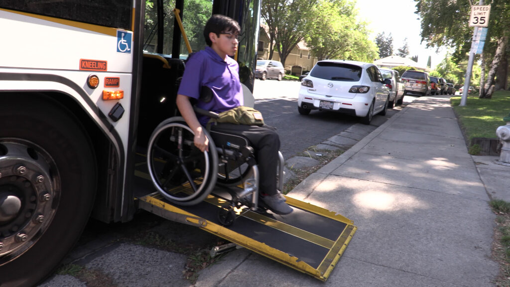 Rider in wheelchair using ramp to exit bus.